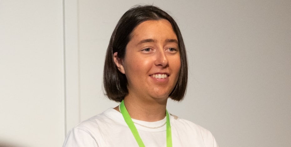 A woman with dark hair in a bob, wearing a white shirt. She has a green lanyard around her neck.