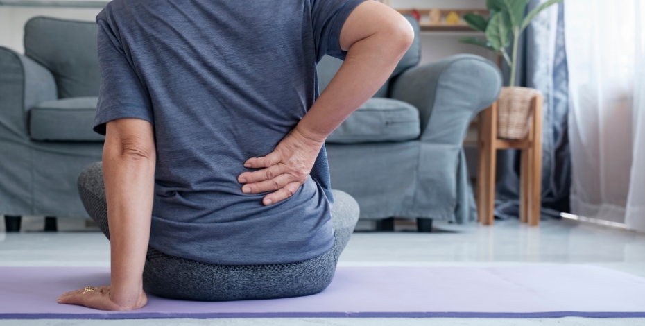 view of the torso or a person sitting on a purple yoga mat holding the right side of their back